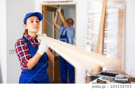 Positive Latin female carpenter in uniform holding wooden planks indoors Positive Latin female carpenter in uniform holding wooden planks indoors 103158703