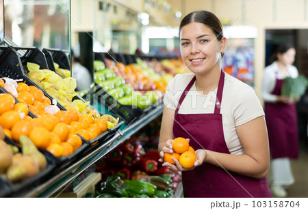Female seller in apron chooses juicy tangerine 103158704