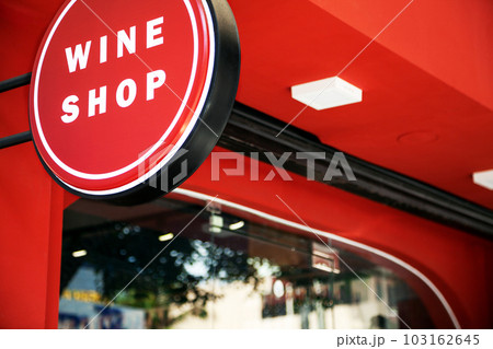 Red and white commercial sign with words Wine Shop on a city street. Alcohol store advertisement lightbox hanging next to the entrance Red and white commercial sign with words Wine Shop on a city street. Alcohol store advertisement lightbox hanging next to the entrance 103162645