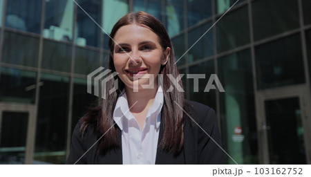 Portrait of a young woman in a black suit looking to camera outside on street. Businesswoman portrait near office building. Portrait of a young woman in a black suit looking to camera outside on street. Businesswoman portrait near office building. 103162752
