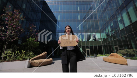 Businesswoman in a black suit holding Need Work sign searching job standing near office centre. Jobless people concept. Global unemployment. 103162796