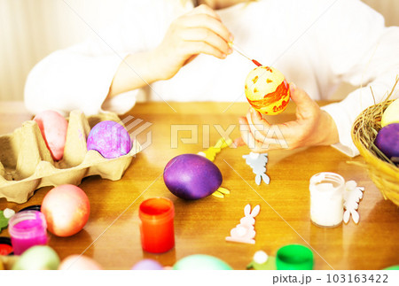 Child hands painting eggs for Easter on the wooden table at home. Preparation for Easter. Child hands painting eggs for Easter on the wooden table at home. Preparation for Easter. 103163422