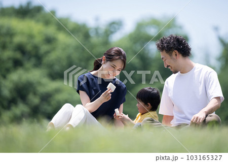 公園の芝生でくつろぐ家族 レジャーシートでサンドイッチを食べる コピースペースあり 公園の芝生でくつろぐ家族 レジャーシートでサンドイッチを食べる コピースペースあり 103165327