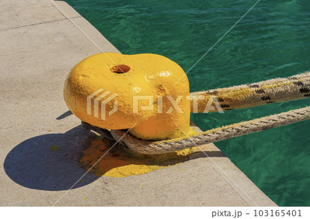 A thick hawser rope used to moor a ship on a yellow pier at the seaport. 103165401
