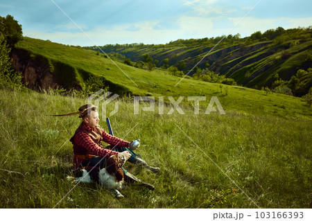 Male hunter in retro suit clothes with hat sitting with dog and waiting for prey animal over picturesque landscapes. Companion dog English springer spaniel Male hunter in retro suit clothes with hat sitting with dog and waiting for prey animal over picturesque landscapes. Companion dog English springer spaniel 103166393
