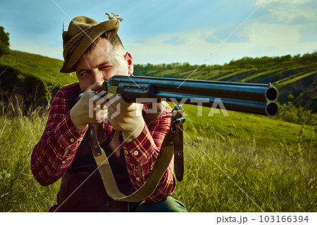 Close up portrait with man, hunter wearing vintage clothes and checked shirt shooting prey with a rifle over marvelous landscapes background 103166394
