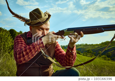 Close up portrait with man, hunter wearing vintage clothes and checked shirt shooting prey with a rifle over marvelous landscapes background 103166396