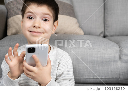 A preschool boy uses a smartphone, plays games on his phone, place for text 103168250