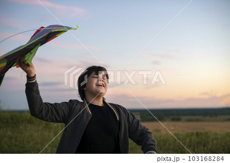 A teenager launches a kite at sunset in the summer in a field. The concept of hobbies, recreation and entertainment A teenager launches a kite at sunset in the summer in a field. The concept of hobbies, recreation and entertainment 103168284