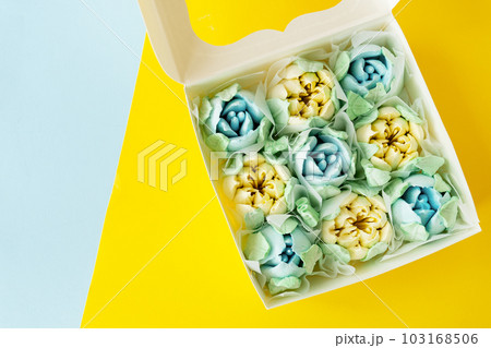 Yellow-blue marshmallow in the form of flowers in the form of tulips. Marshmallow in a box on a yellow-blue background. View from above. 103168506