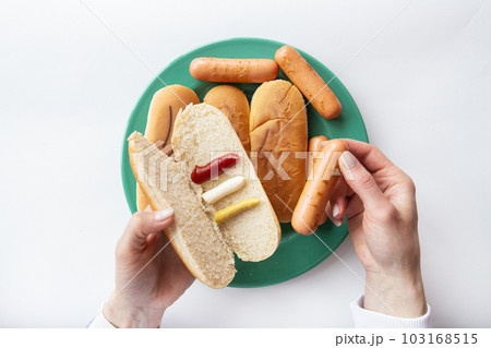 Fresh hot dog buns which lie on a green plate along with sausages. The girl holds in her hands a bun with sauces in which she puts a sausage. Fresh hot dog buns which lie on a green plate along with sausages. The girl holds in her hands a bun with sauces in which she puts a sausage. 103168515