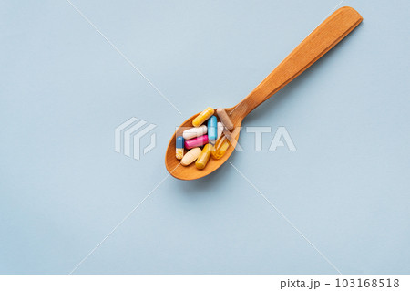 Various bright pills on a blue background lie in a wooden spoon. The concept of healthcare and evidence-based medicine, close-up. Various bright pills on a blue background lie in a wooden spoon. The concept of healthcare and evidence-based medicine, close-up. 103168518