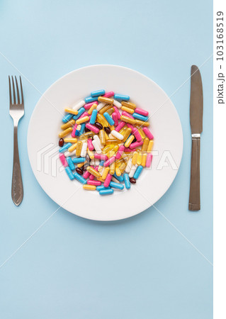 Tablets, capsules, vitamins and natural organic food supplements on a white plate on a blue background. Minimal modern pharmacy or healthcare concept. Vertical photo. Tablets, capsules, vitamins and natural organic food supplements on a white plate on a blue background. Minimal modern pharmacy or healthcare concept. Vertical photo. 103168519