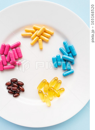 Food supplements of bright color lie on a white plate on a blue background. Concept of health support and lack of vitamins. Vertical photo. Food supplements of bright color lie on a white plate on a blue background. Concept of health support and lack of vitamins. Vertical photo. 103168520