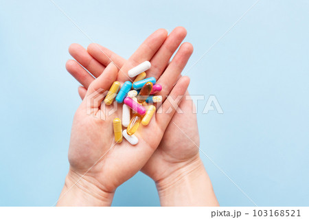 The girl holds a handful of brightly colored vitamins, nutritional supplements, and medicines in her palms. Concept of medicine and health support. 103168521