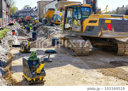 Street reconstruction site with workers, excavators, vibratory plate compactors and other machinery 103169529
