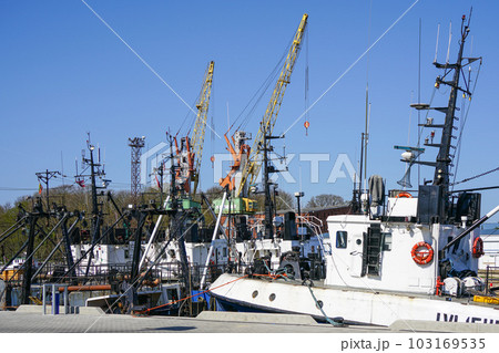 Colorful harbor pier view with small fishing vessels and harbor cranes on blue sky background 103169535