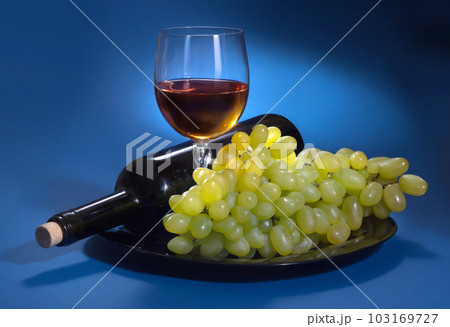 A bottle of grape wine and white grapes on a blue background A bottle of grape wine and white grapes on a blue background 103169727