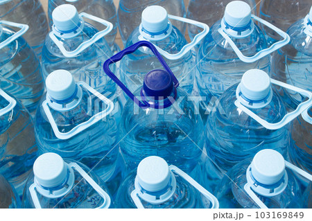 Many blue plastic bottles with blue caps and one with dark blue cap with clear mineral water in a supermarket. Pure filtered ecologically clean water in packaging. Close Up. One is different from all Many blue plastic bottles with blue caps and one with dark blue cap with clear mineral water in a supermarket. Pure filtered ecologically clean water in packaging. Close Up. One is different from all 103169849