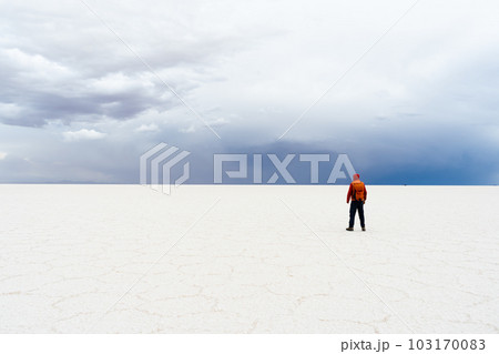 Traveler Man with Backpack Standing at Uyuni Salt Flats on Cloudy Day. Altiplano, Bolivia. Salt 103170083