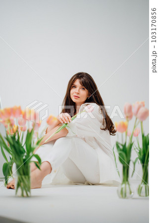 gentle brunette in white sits on the floor with vases of tulips 103170856