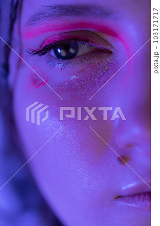 Half young female face with shiny stage make-up with sparkles and arrows illuminated with blue and pink neon light. Studio shot of Caucasian ethnicity adult woman looking away. Part of photo series 103171717