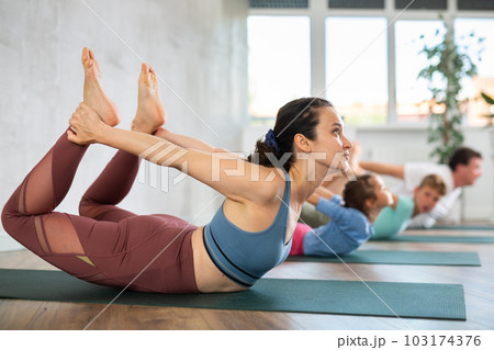 Willing middle-aged woman practicing bow pose of yoga with her family 103174376