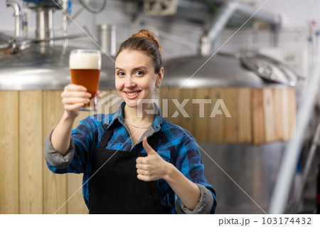 Portrait of female brewer who is standing with glass of beer on his workplace in brew-house 103174432
