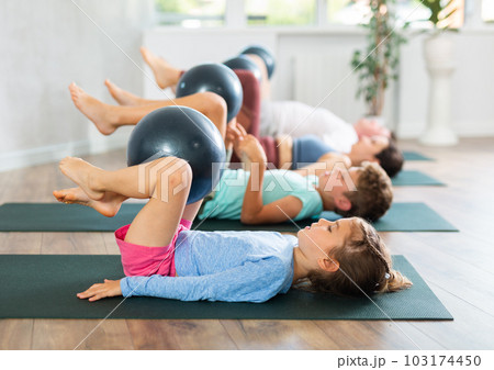 Children and parents practice yoga and Pilates using soft ball in gym Children and parents practice yoga and Pilates using soft ball in gym 103174450