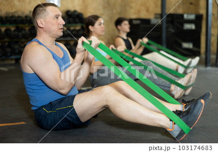 Active middle-aged man wearing sport clothes using resistance band during group workout in gym Active middle-aged man wearing sport clothes using resistance band during group workout in gym 103174683
