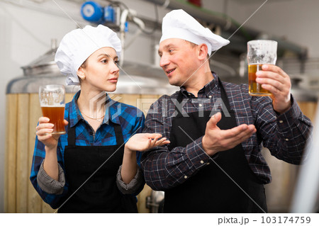 Woman and man brewmasters checking quality of beer and discussing 103174759