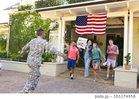 Happy diverse group of friends greeting biracial male american soldier outside the house 103174956