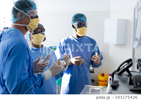 Diverse group of surgeons discussing x rays on screen in operating theatre 103175426