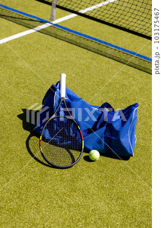Tennis racket, ball and sports bag on the ground by net on sunny outdoor grass court, copy space Tennis racket, ball and sports bag on the ground by net on sunny outdoor grass court, copy space 103175467