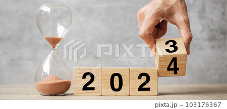 hand flipping block 2023 to 2024 text with hourglass on table. Resolution, time, plan, goal, motivation, reboot, countdown  and New Year holiday concepts 103176367