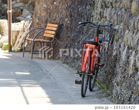 石壁に立てかけられた赤い自転車とベンチ 石壁に立てかけられた赤い自転車とベンチ 103181420