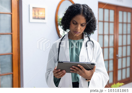 Biracial female doctor wearing sthethoscope, using tablet at doctor's office Biracial female doctor wearing sthethoscope, using tablet at doctor's office 103181865