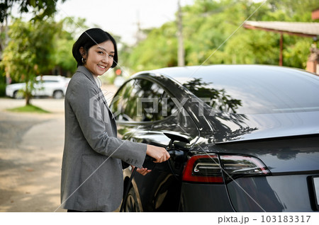 A successful Asian businesswoman charging her electric car at a public charger station. 103183317