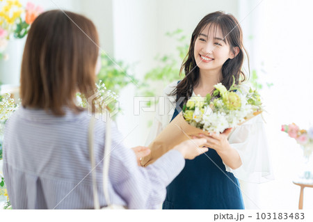 フラワーショップで花束をお客に渡す若い女性の店員 フラワーショップで花束をお客に渡す若い女性の店員 103183483