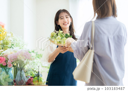 フラワーショップで花束をお客に渡す若い女性の店員 フラワーショップで花束をお客に渡す若い女性の店員 103183487