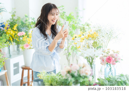 フラワーショップでスマホで撮影をする若い女性の店員 フラワーショップでスマホで撮影をする若い女性の店員 103183518