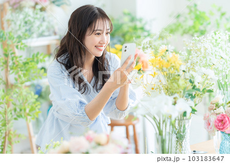 フラワーショップでスマホで撮影をする若い女性の店員 103183647