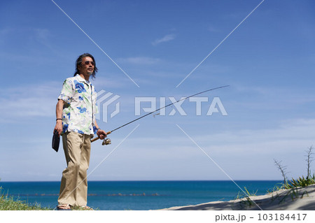 青空のもと釣り竿を持って立つミドルシニア男性 103184417