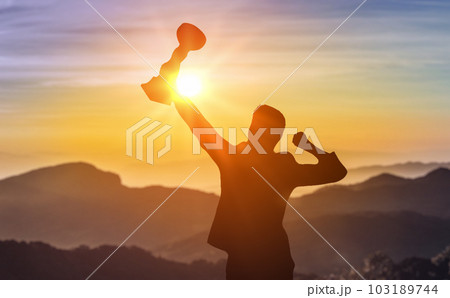 Silhouette of businessman celebrating raising arms on top of mountain with over blue sky and sunlight. concept of leadership successful achievement with goal, growth up, win and objective target. 103189744