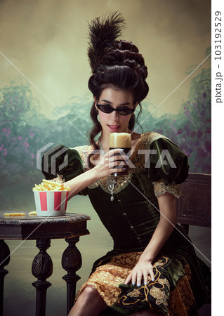 Portrait of beautfiufl young girl, princess in elegant drss and sunglasss drinking foamy beer, eating fries against dark vintage background 103192529