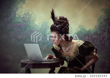 Misunderstanding. Young beautiful woman, royal person in elegant dress looking on laptop with funny face against dark vintage background 103192543