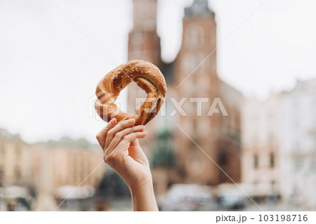 Tourist is holding prezel, traditional polish snack on the Market square in Krakow. Traveling Europe in spring. Food banner Tourist is holding prezel, traditional polish snack on the Market square in Krakow. Traveling Europe in spring. Food banner 103198716