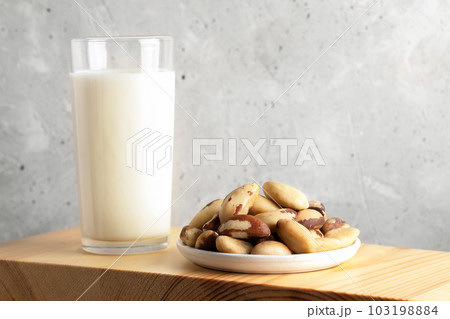 One glass of vegan milk made of brazil nut and nuts in plate on wooden board. Close up. Copy space. One glass of vegan milk made of brazil nut and nuts in plate on wooden board. Close up. Copy space. 103198884