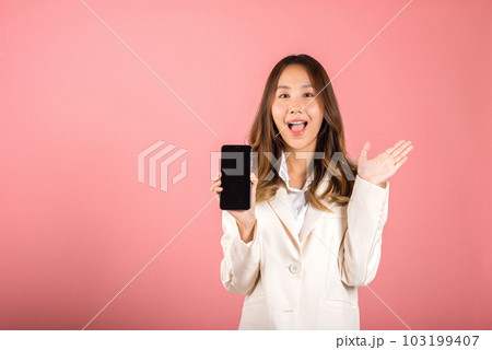 Happy Asian portrait beautiful cute young woman teen smiling excited holding blank screen mobile phone studio shot isolated on pink background, Thai female person showing smartphone empty screen space Happy Asian portrait beautiful cute young woman teen smiling excited holding blank screen mobile phone studio shot isolated on pink background, Thai female person showing smartphone empty screen space 103199407