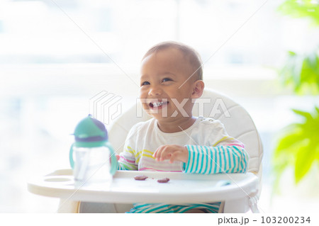Baby eating solid foods in high chair. Baby eating solid foods in high chair. 103200234